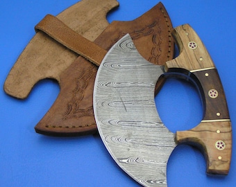 Op de afbeelding: Een Damascus stalen cleaver met een houten handvat en een leren schede. Het handvat heeft een decoratieve inleg van hout en metaal. De cleaver is een uniek en prachtig stuk vakmanschap.