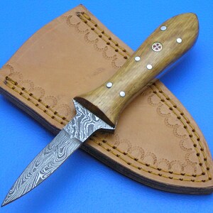 May include: A small,  damascus steel knife with a wooden handle and a leather sheath. The handle has a red and gold inlay and silver accents.