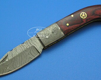 May include: A small pocket knife with a patterned steel blade and a red wood handle. The handle has gold accents and a decorative circle.