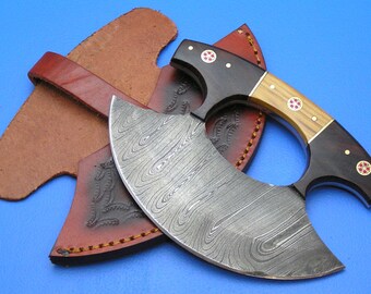 Op de afbeelding: Een Damascus stalen cleaver met een houten handvat en een leren schede. Het handvat heeft rode en gouden accenten. Het blad is gebogen en heeft een uniek patroon.