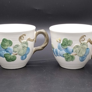 Peut inclure: Ensemble de quatre tasses à thé en céramique blanche avec des poignées brunes. Chaque tasse présente un motif de vigne avec des raisins bleus et des feuilles vertes.