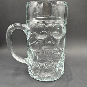 Puede incluir: Un jarro de cerveza de vidrio transparente con asa y un diseño texturizado con burbujas.