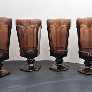 May include: Four brown glass goblets with a footed base. The goblets are clear and have a textured design.