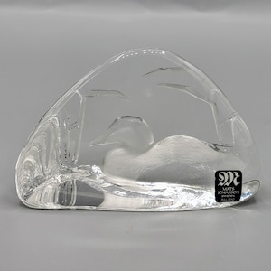 May include: A clear glass sculpture of a loon resting on a branch, with a signature from Mats Jonasson Sweden on the bottom.