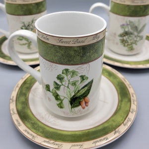 May include: Set of three white ceramic mugs with green and brown floral designs. Each mug features a different herb with its name written on the mug. The mugs are on matching saucers with the same design.