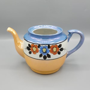 Peut inclure: Une petite théière bleue et orange avec des motifs floraux. La théière a une poignée et un bec.