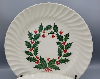 May include: Two white ceramic dinner plates with a green holly leaf and red berry wreath design. The plates have a scalloped edge.