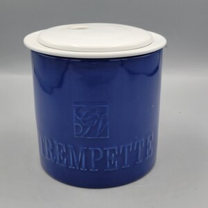 Könnte beinhalten: Eine blaue Keramikdose mit einem weißen Deckel und dem Wort "CREMPETTE" in Prägung auf der Seite. Die Dose hat ein dekoratives Design auf der Vorderseite.