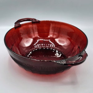 Könnte beinhalten: Eine rote Glasschüssel mit zwei Griffen. Die Schüssel hat ein strukturiertes, geripptes Design und eine klare, glänzende Oberfläche.
