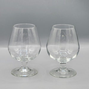 May include: Two clear glass brandy snifters with a round base and a wide bowl.