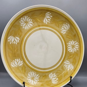 Pode incluir: Um prato grande, redondo, de cerâmica amarela com um centro branco e um desenho floral branco ao redor da borda.