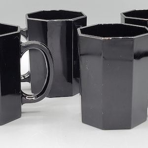 May include: Four black octagonal mugs with handles. The mugs are made of glass and have a smooth, glossy finish.