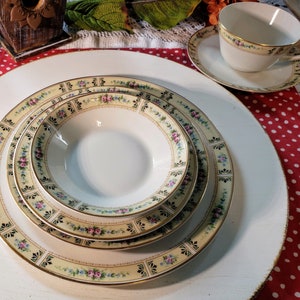 Puede incluir: Un juego de cuatro platos de porcelana blanca con un patrón floral en tonos de rosa, azul y verde. Los platos tienen un borde dorado y están dispuestos en forma anidada, con el plato más grande en la parte inferior y el plato más pequeño en la parte superior.