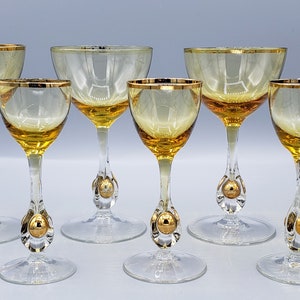 Può includere: Set di sette bicchieri da vino in vetro ambrato con bordo dorato e dettagli a sfera dorata sui gambi.