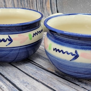 Puede incluir: Tres tazones de sopa de cerámica azul y blanca con asas. Los tazones tienen un interior blanco y un exterior azul con un diseño floral blanco y rosa.