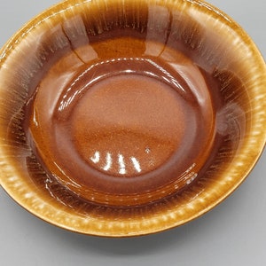 Könnte beinhalten: Eine braune Keramikschüssel mit glasierter Oberfläche. Die Schüssel hat einen breiten Rand und einen glatten, abgerundeten Innenraum.