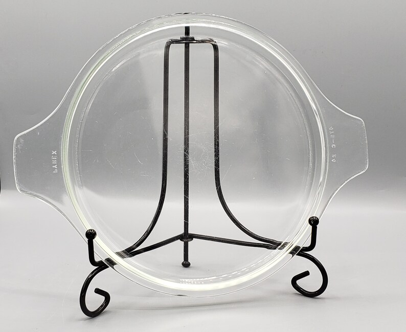 May include: A clear glass lid with a black metal stand. The lid has a raised edge and is marked "LAMBEX" and "SIZE-C 6.5".