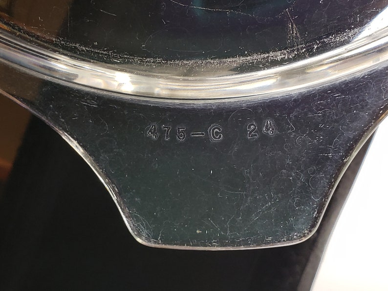 May include: Close-up of the bottom of a black pot with a silver rim. The pot has the numbers "475-C 24" printed on the bottom.