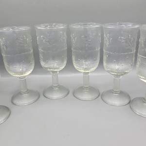 May include: Set of six clear glass wine glasses with a textured, frosted finish. The glasses have a round bowl and a stem.