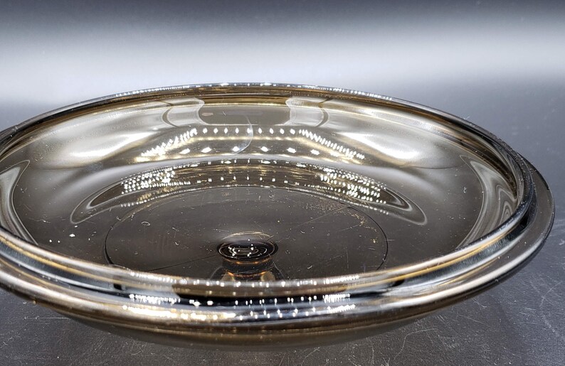 May include: A clear glass bowl with a dark brown tint. The bowl has a wide, shallow shape and a smooth, reflective surface.