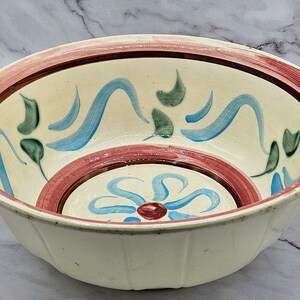 Peut inclure: Un bol en céramique blanche avec un motif floral rose, brun et bleu. Le bol a un bord festonné et est parfait pour servir des salades, des fruits ou des en-cas.