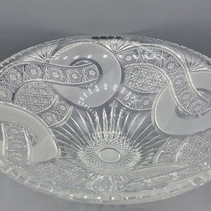 May include: A large, clear glass bowl with a decorative, cut-glass pattern. The bowl has a wide, shallow shape and a scalloped edge.