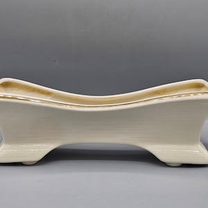 May include: A white ceramic planter with a gold trim, shaped like a long, narrow trough with two legs on either side.