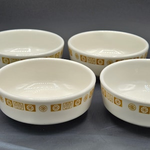 Puede incluir: Juego de cuatro cuencos de cerámica blanca con un patrón geométrico dorado. Los cuencos son redondos y tienen un ligero borde.