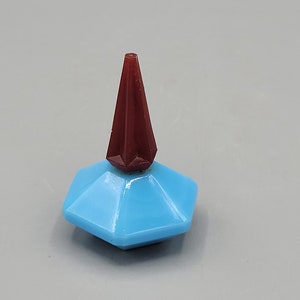 May include: A small, blue glass perfume bottle with a red, pointed stopper.