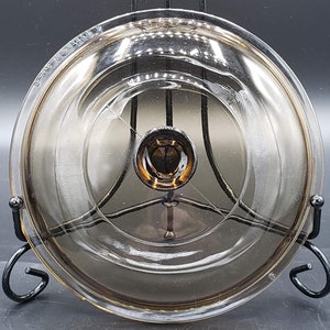 May include: A clear glass lid with a brown tint and a metal knob. The lid is on a black metal stand.