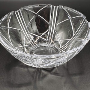 May include: A clear glass bowl with a geometric pattern. The bowl has a wide, shallow shape and a smooth, polished finish.
