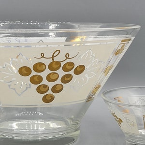 Puede incluir: Un juego de dos cuencos de vidrio con fondo blanco y detalles dorados. Los cuencos presentan un diseño de uvas con hojas y uvas doradas.