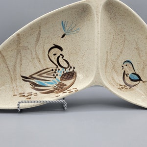 Puede incluir: Un plato de servir dividido con un diseño de pájaro marrón y azul. El plato está hecho de cerámica y tiene un esmalte moteado. El plato tiene forma de media luna.