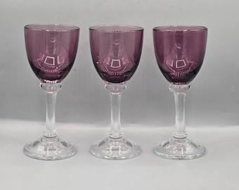 Op de afbeelding: Drie glazen wijnbekers van helder glas met paars getinte kommen. De bekers hebben een steel.
