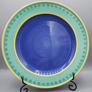May include: A blue ceramic dinner plate with a yellow and green rim. The rim has a dotted pattern.