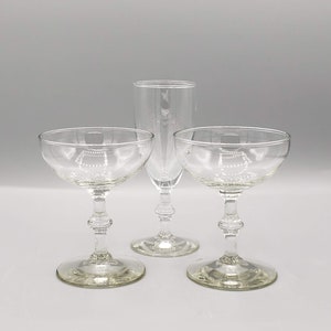 May include: Three clear glass champagne coupes, two with a stemmed base and one with a tall, slender stem.