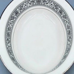 Może przedstawiać: Biała ceramiczna miska z czarno-srebrną ozdobną obwódką. Obwódka ma powtarzający się wzór kwiatowy.