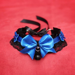 May include: A black choker with a blue satin bow and a bell charm. The choker is made of lace and ribbon.
