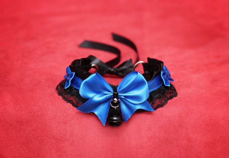 May include: A black choker with a blue satin bow and a bell charm. The choker is made of lace and ribbon.