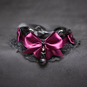 May include: A black lace choker with a large burgundy satin bow and a silver bell charm.