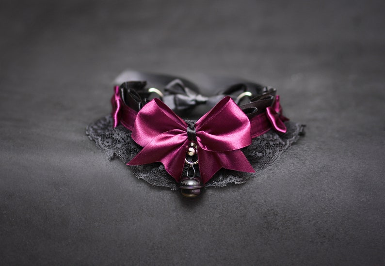 May include: A black lace choker with a large burgundy satin bow and a silver bell charm.