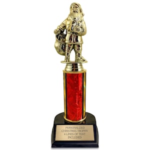 May include: A gold-colored Santa Claus trophy with a red and gold column and a black base. The trophy has a gold plaque with the text "PERSONALIZED CHRISTMAS TROPHY 4 LINES OF TEXT INCLUDED".