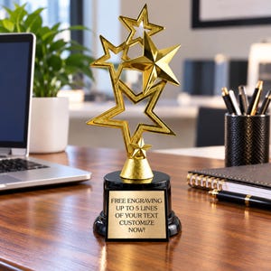 May include: A gold-colored star trophy featuring multiple star shapes stacked vertically on a black circular base. The base includes a rectangular plate with the text: FREE ENGRAVING UP TO 5 LINES OF YOUR TEXT CUSTOMIZE NOW!