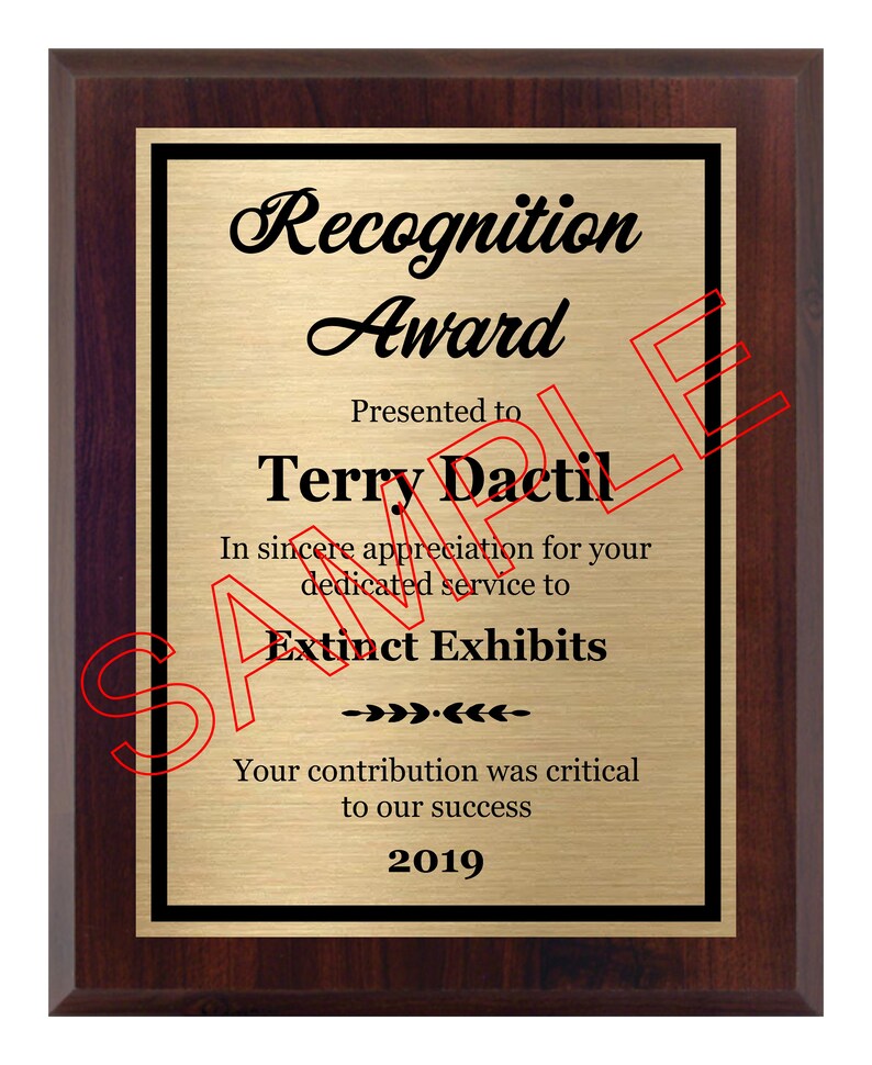 May include: A mahogany-colored plaque with a gold-colored plate. The plaque has a black border and the text "Recognition Award" in a black cursive font. The text "Presented to Terry Dactil" is in black text. The text "In sincere appreciation for your dedicated service to Extinct Exhibits" is in black text. The text "Your contribution was critical to our success" is in black text. The text "2019" is in black text.