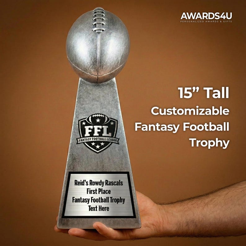 May include: A silver-colored fantasy football trophy, 15 inches tall, with a football-shaped top. The trophy features the text "FFL Fantasy Football League" and is customizable with text. The base reads "Reid's Rowdy Rascals First Place Fantasy Football Trophy Text Here."