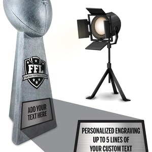 May include: A gray football-shaped trophy with the text "FFL Fantasy Football League" and "Add Your Text Here". The image also includes a spotlight and text that reads "Free Engraving" and "Personalized Engraving".