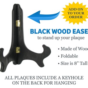 May include: Black wooden easel for displaying plaques. It is foldable and measures 8 inches tall. The easel is made of wood and has a keyhole on the back for hanging.