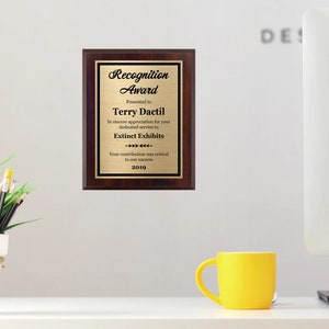 May include: A gold plaque with a mahogany frame recognizes Terry Dactil for their dedicated service to Extinet Exhibits. The plaque reads "Recognition Award" and includes the year 2019.