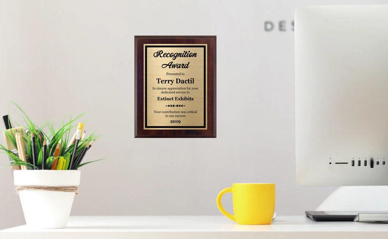 May include: A gold plaque with a mahogany frame recognizes Terry Dactil for their dedicated service to Extinet Exhibits. The plaque reads "Recognition Award" and includes the year 2019.