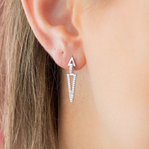 May include: A pair of silver earrings with a geometric design. The earrings are made of small, clear stones that are set in a triangle shape. The earrings are hanging from a small, silver post.